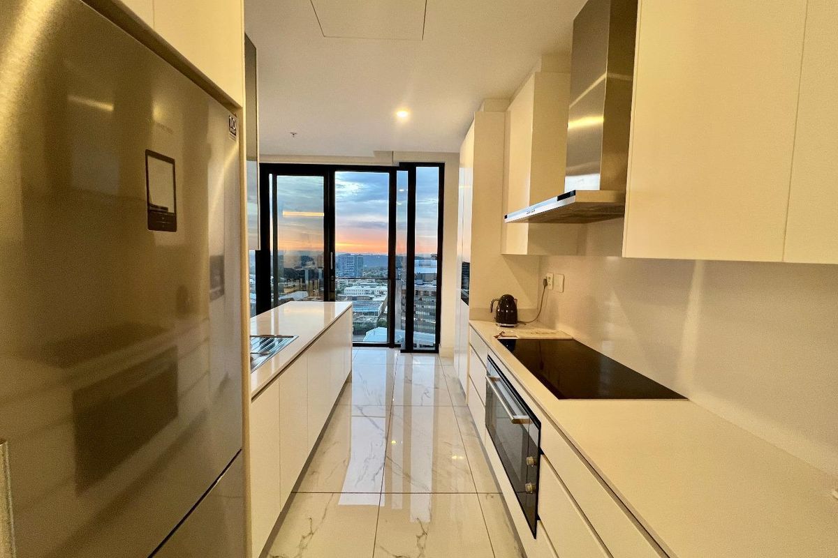 Modern galley-style kitchen featuring sleek white cabinetry, integrated appliances, a glass cooktop, and polished marble-look floor tiles with a scenic city view.
