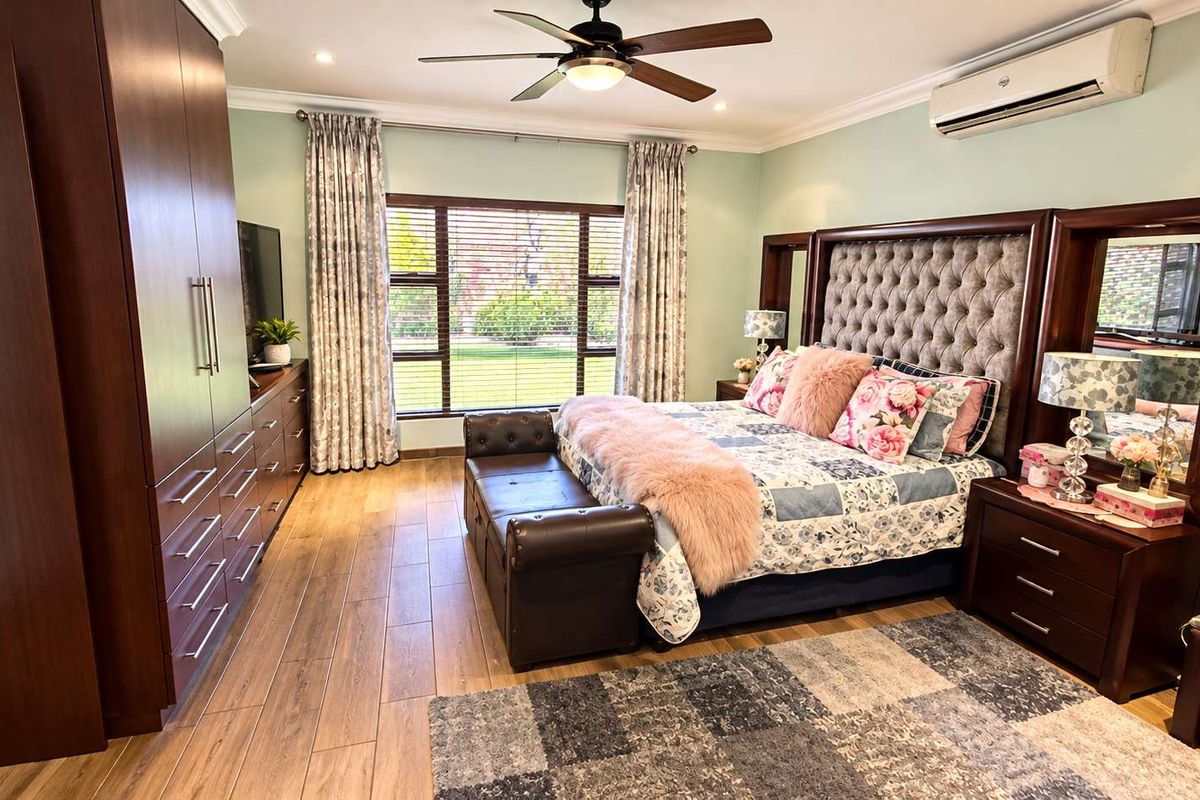 Spacious bedroom featuring wood-look tile flooring, built-in cupboards, a ceiling fan, and a wall-mounted air conditioning unit.