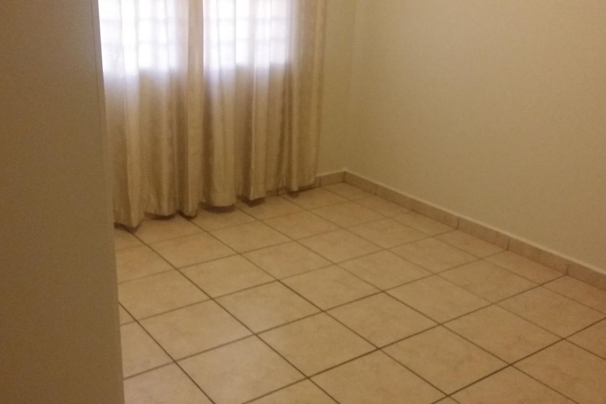 An empty bedroom featuring neutral tiled flooring and simple window treatments, offering a blank canvas for personalization.