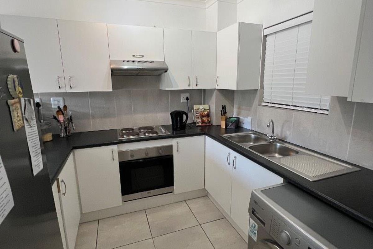 A functional kitchen featuring white cabinetry, dark countertops, a built-in oven, hob, extractor fan, and a double stainless steel sink with tiled flooring.
