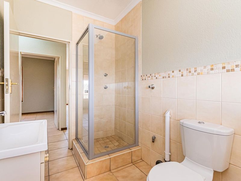 A functional bathroom featuring a glass shower enclosure, toilet, and washbasin with neutral wall and floor tiling.