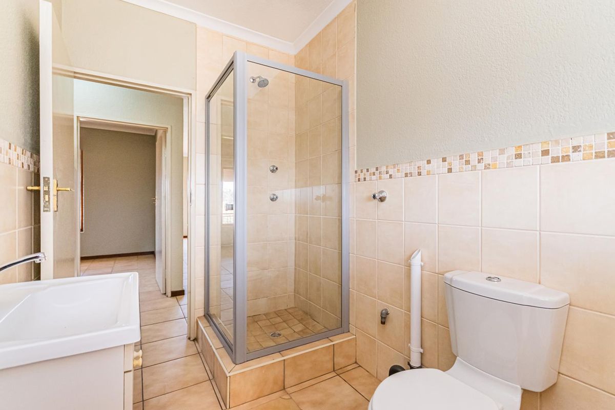 A functional bathroom featuring a glass shower enclosure, toilet, and washbasin with neutral wall and floor tiling.