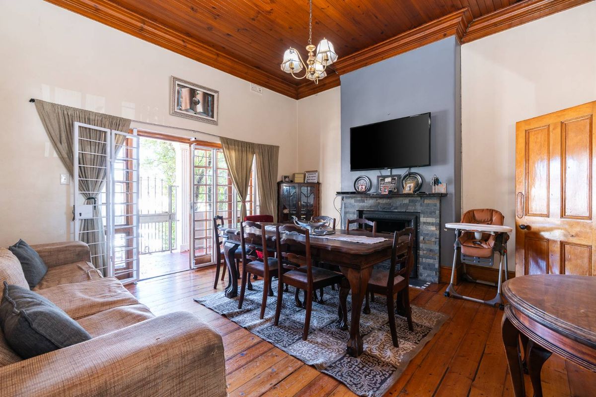 Spacious living and dining area featuring high timber ceilings, original timber flooring, and a stone-surround fireplace with direct access to an outdoor patio.