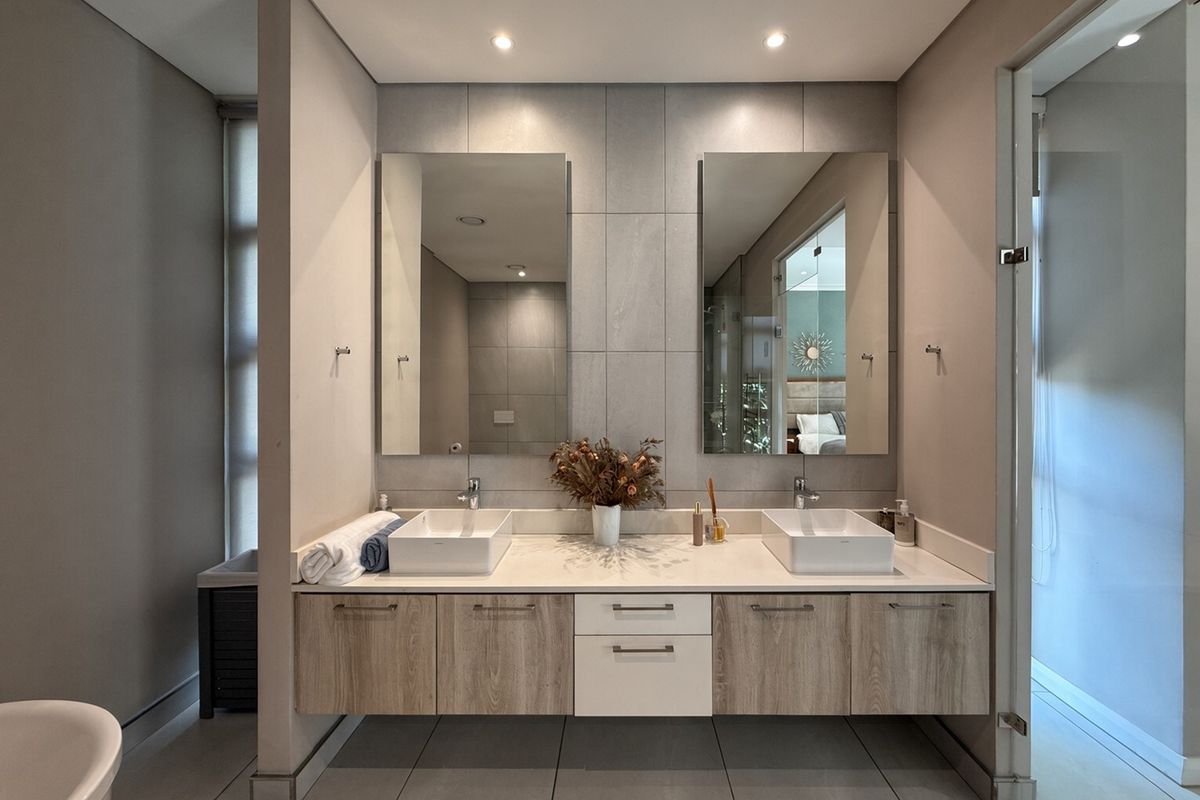Modern bathroom featuring a double vanity with vessel sinks, floating cabinetry, large wall-mounted mirrors, and contemporary grey tiling.