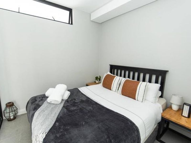 A modern bedroom featuring neutral walls, tiled flooring, and a high-positioned clerestory window providing natural light.