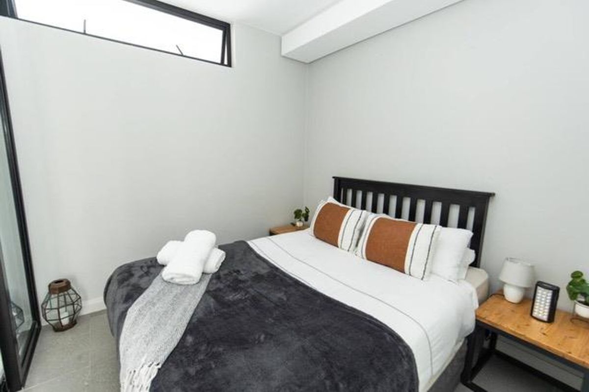 A modern bedroom featuring neutral walls, tiled flooring, and a high-positioned clerestory window providing natural light.