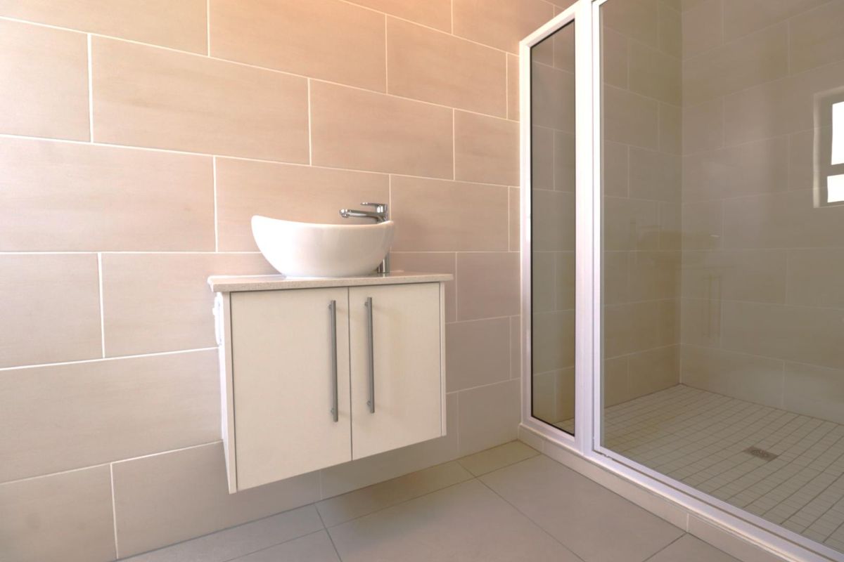 Modern bathroom featuring a wall-mounted vanity with a vessel sink and a glass-enclosed walk-in shower with neutral wall tiling.