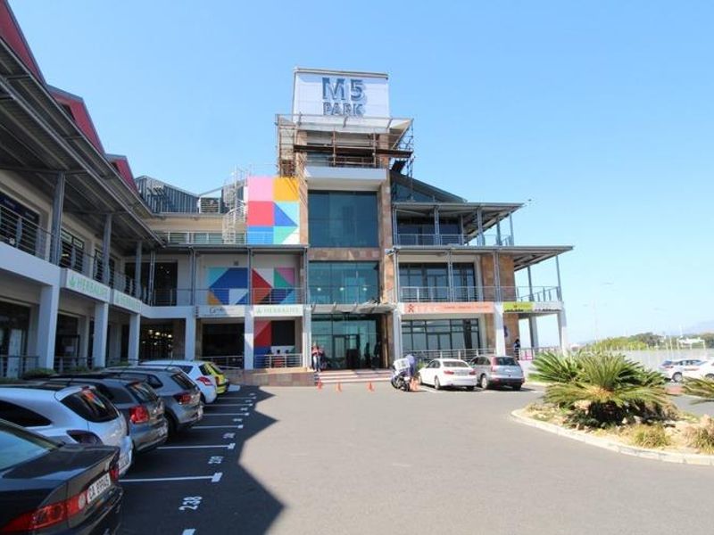 Front exterior view of M5 Park, a multi-story commercial building featuring glass facades, stone cladding, and an integrated parking area.