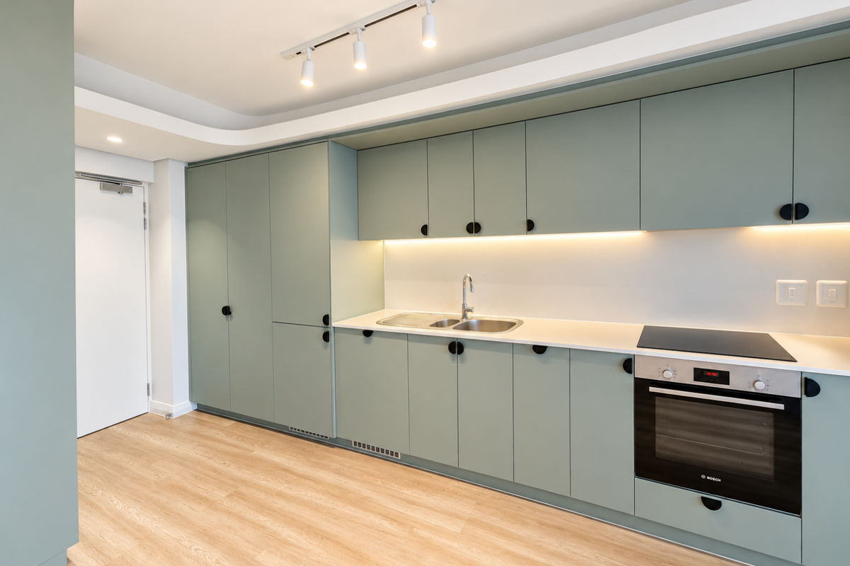 Modern kitchen featuring sage green cabinetry, integrated Bosch oven, electric hob, stainless steel sink, and sleek under-cabinet lighting with light wood-look flooring.