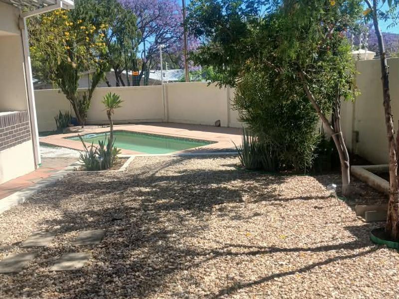 A private backyard featuring a swimming pool with a paved surround and low-maintenance gravel landscaping enclosed by a perimeter wall.