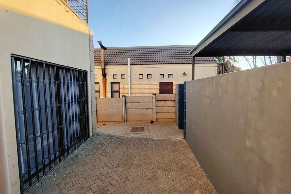 A paved rear courtyard area featuring a security gate, perimeter walling, and a covered section, providing a functional outdoor space.
