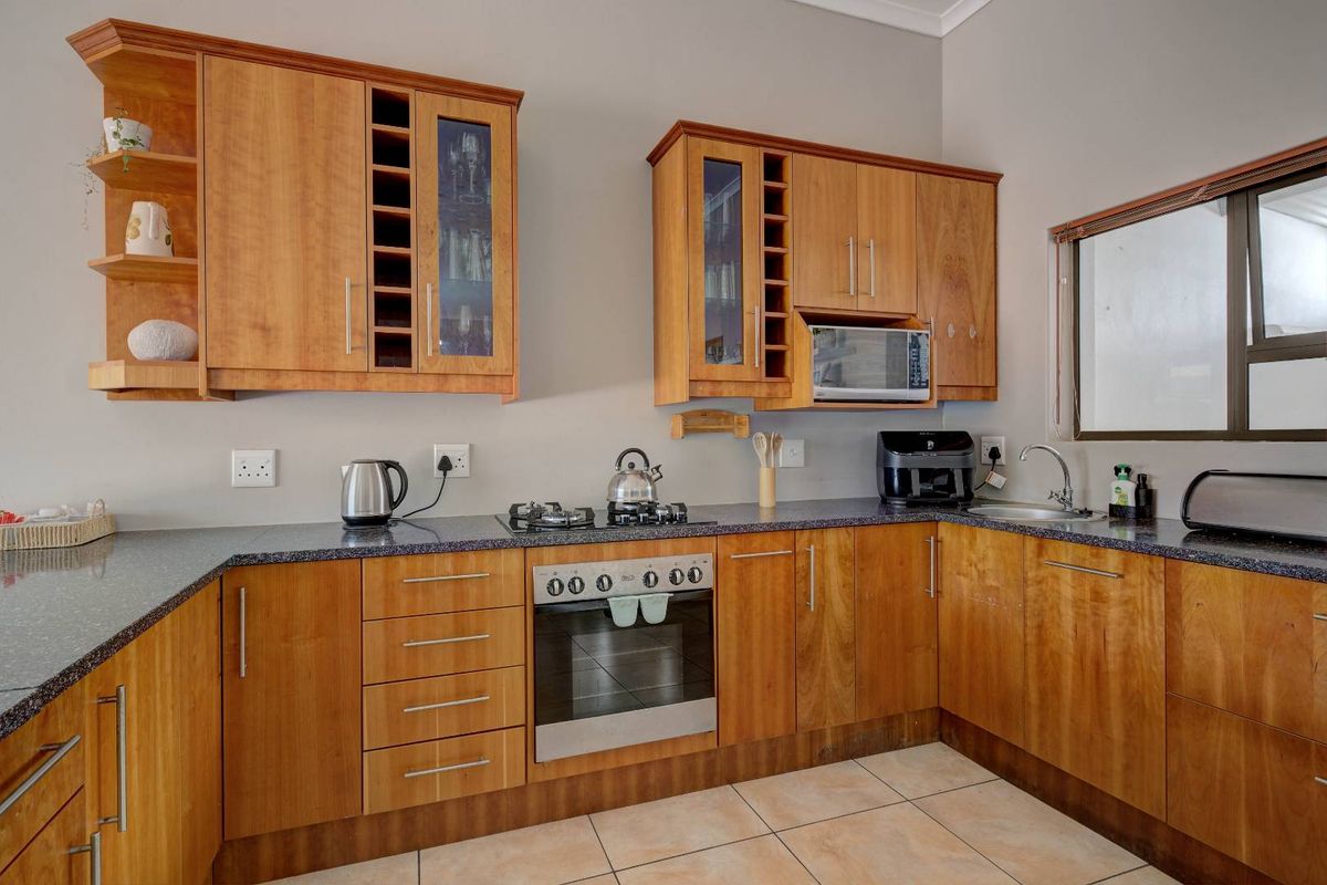 A functional kitchen featuring warm-toned wooden cabinetry, granite countertops, a built-in oven, gas hob, and a stainless steel sink.