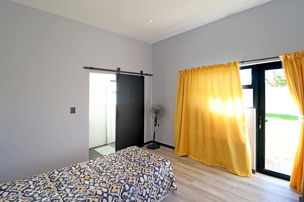 A bright bedroom featuring light wood-look flooring, a sliding barn door leading to an en-suite bathroom, and direct access to the garden.