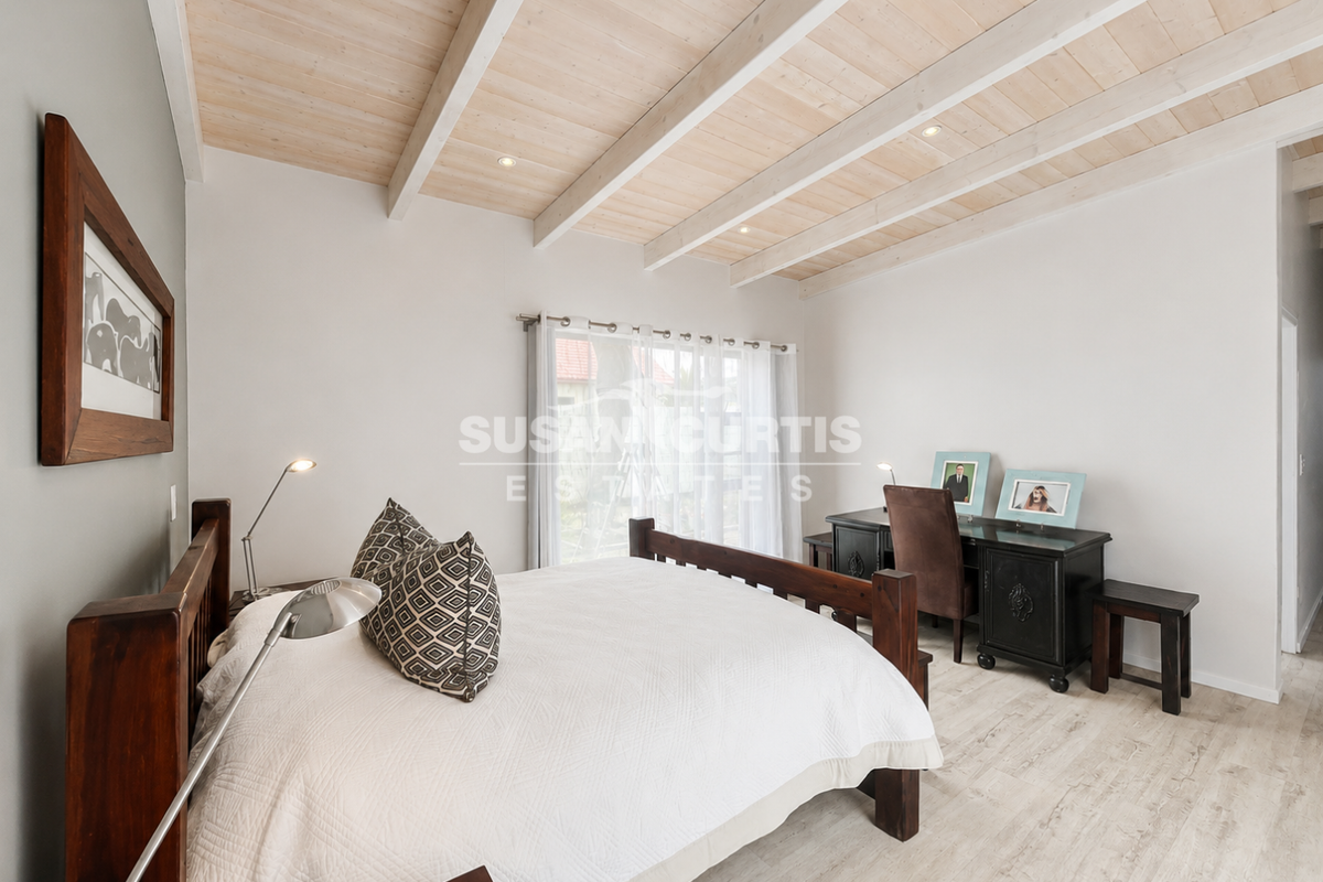 Spacious bedroom featuring a high exposed timber beam ceiling, recessed lighting, and light-toned laminate flooring with direct access to the exterior.