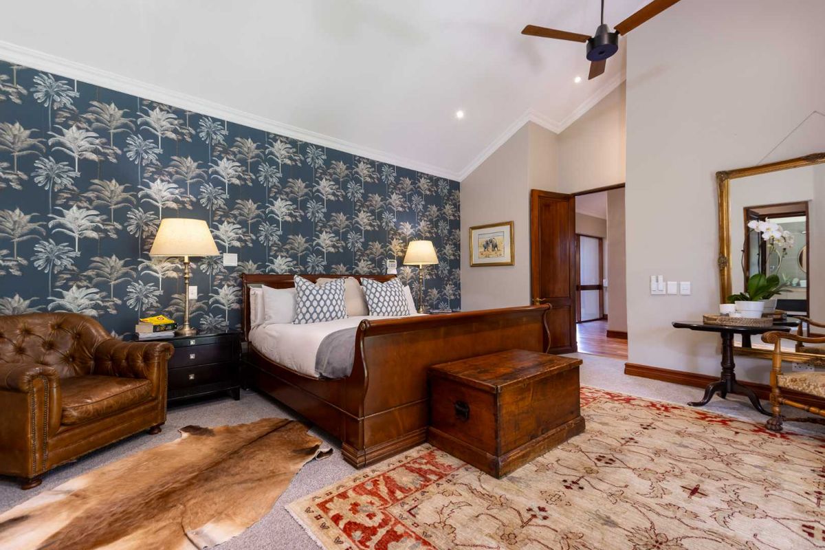 Spacious bedroom featuring a vaulted ceiling, ceiling fan, and a striking palm-patterned feature wall, offering a comfortable and well-maintained living space.