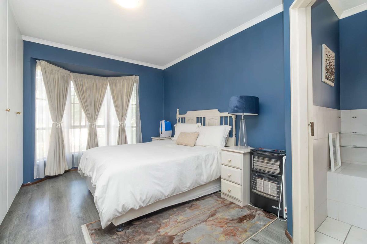 A bedroom featuring blue painted walls, laminate flooring, and a bay window with built-in wardrobe storage.