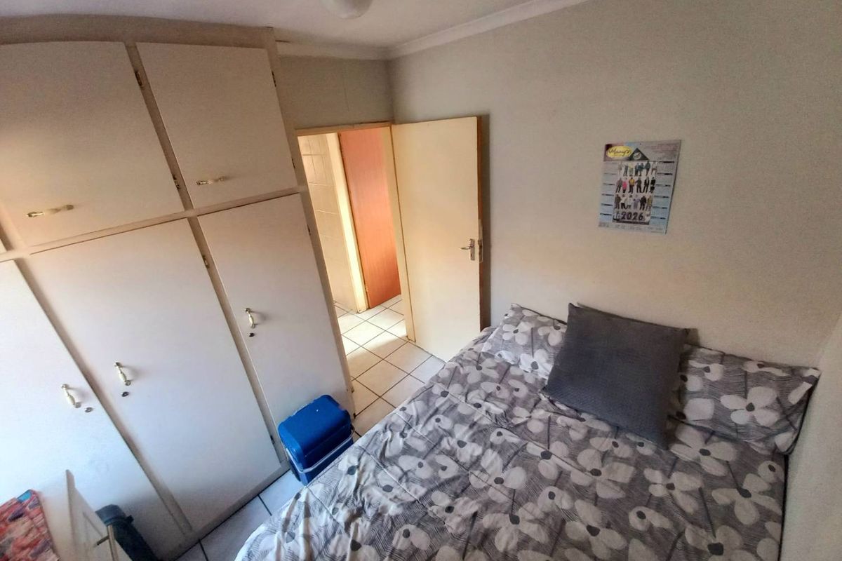 A functional bedroom featuring built-in cupboards and tiled flooring, with an adjacent doorway leading to a hallway.