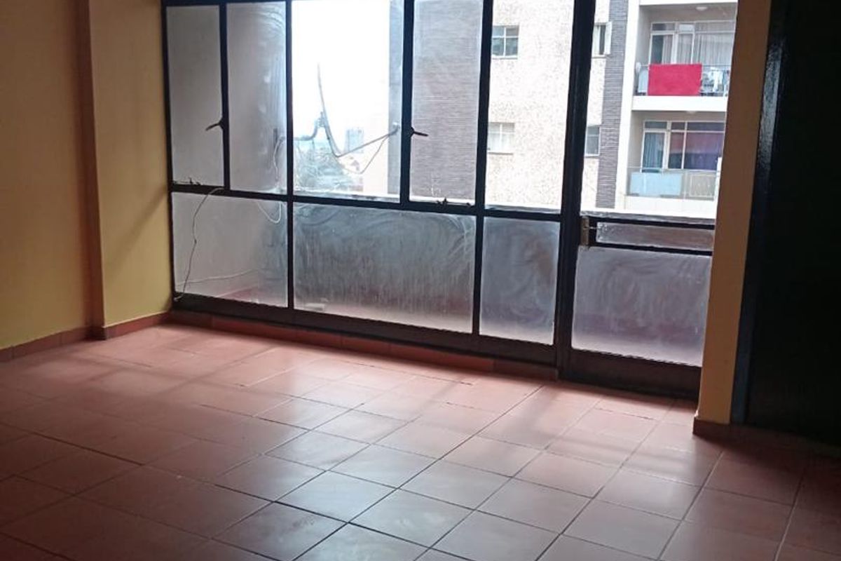 An empty living room featuring tiled flooring and a large metal-framed window with access to an external balcony area.