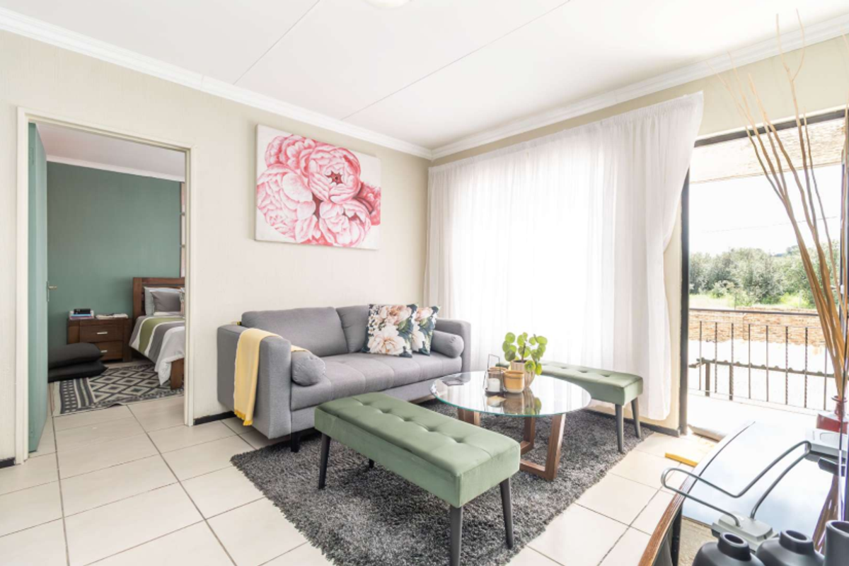 A bright living room featuring tiled flooring, coved ceilings, and a sliding glass door providing access to an outdoor balcony area.
