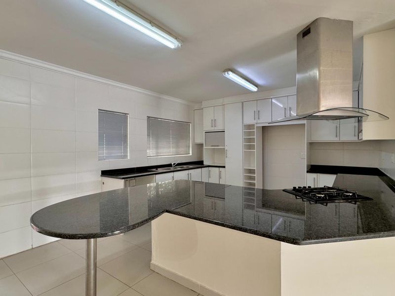 A spacious, modern kitchen featuring granite countertops, a breakfast nook, built-in cabinetry, a gas hob, and a stainless steel extractor fan.