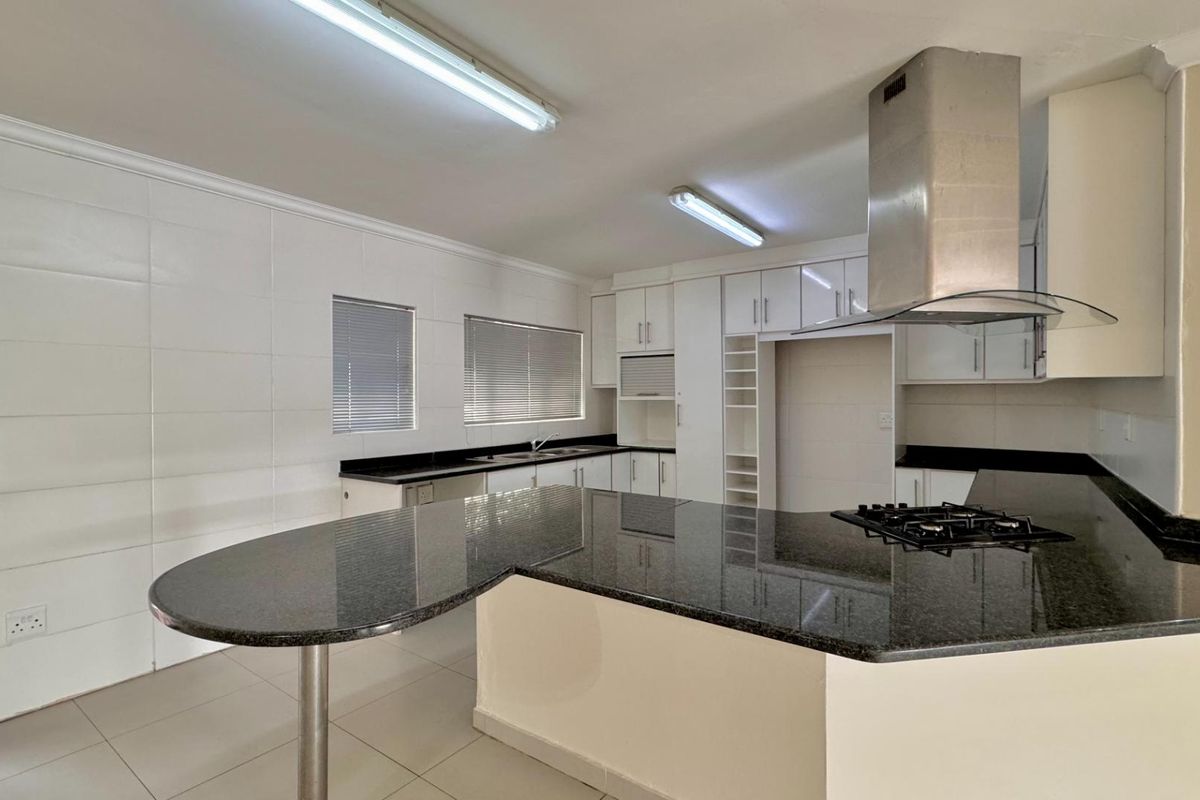 A spacious, modern kitchen featuring granite countertops, a breakfast nook, built-in cabinetry, a gas hob, and a stainless steel extractor fan.