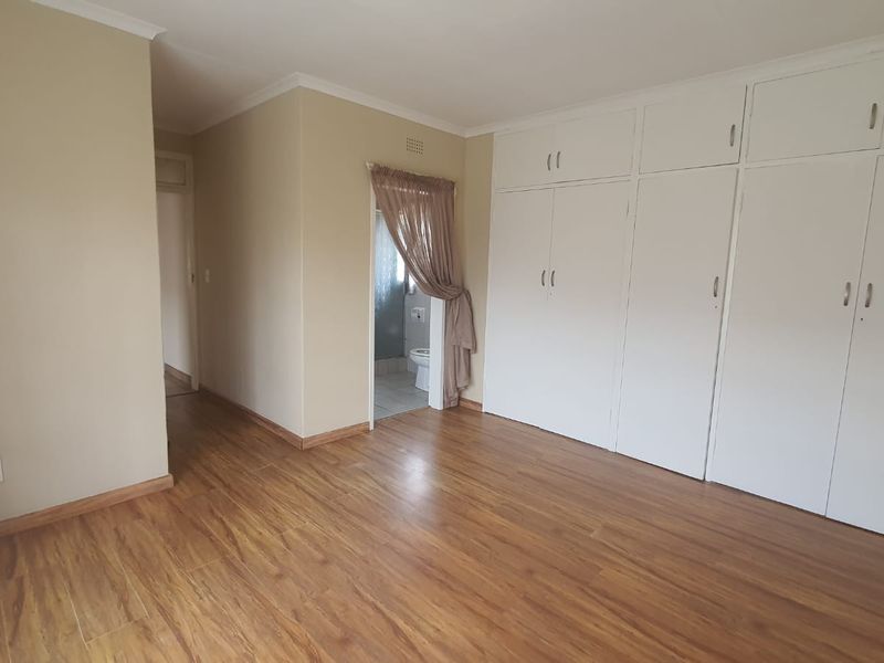 A spacious bedroom featuring laminate flooring, extensive built-in cupboards, and direct access to an en-suite bathroom.