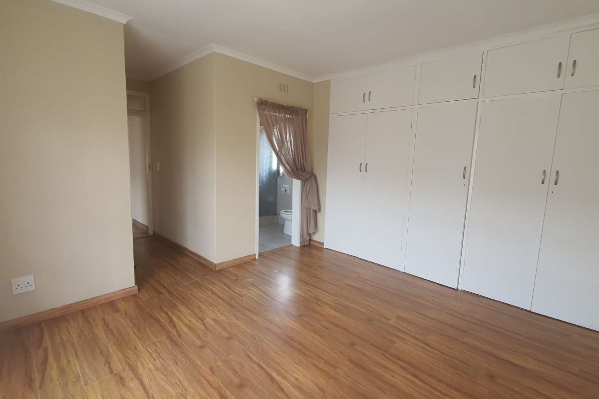 A spacious bedroom featuring laminate flooring, extensive built-in cupboards, and direct access to an en-suite bathroom.