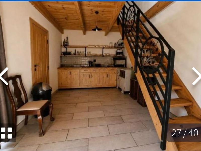 A rustic kitchen area featuring wooden cabinetry, open shelving, subway tile backsplash, and a prominent wooden staircase with a decorative wrought iron railing.