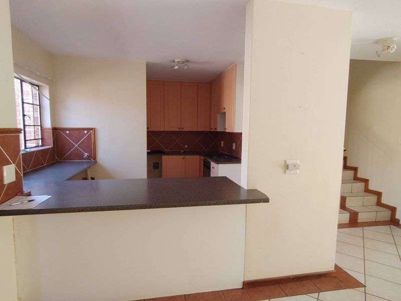 Open plan kitchen area featuring built-in cabinetry, laminate countertops, and tiled flooring, adjacent to a staircase leading to the upper level.