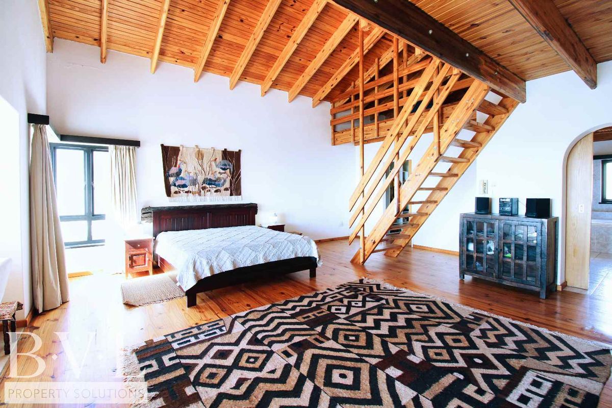 Spacious bedroom featuring high vaulted timber ceilings, exposed wooden beams, and a mezzanine level accessible via a wooden staircase.