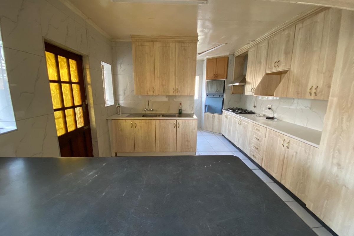 A functional kitchen featuring light wood-finish cabinetry, built-in oven, gas hob, extractor fan, and tiled surfaces throughout.