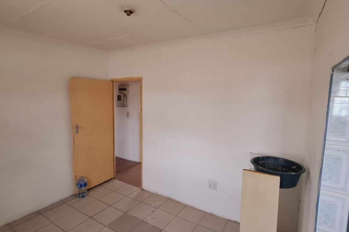 A basic, empty kitchen area featuring tiled flooring and a visible electrical distribution board, requiring cosmetic updates and repairs to finishes.