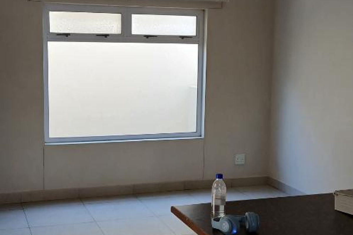A bright, empty living area featuring neutral tiled flooring, a large window, and a built-in counter space.