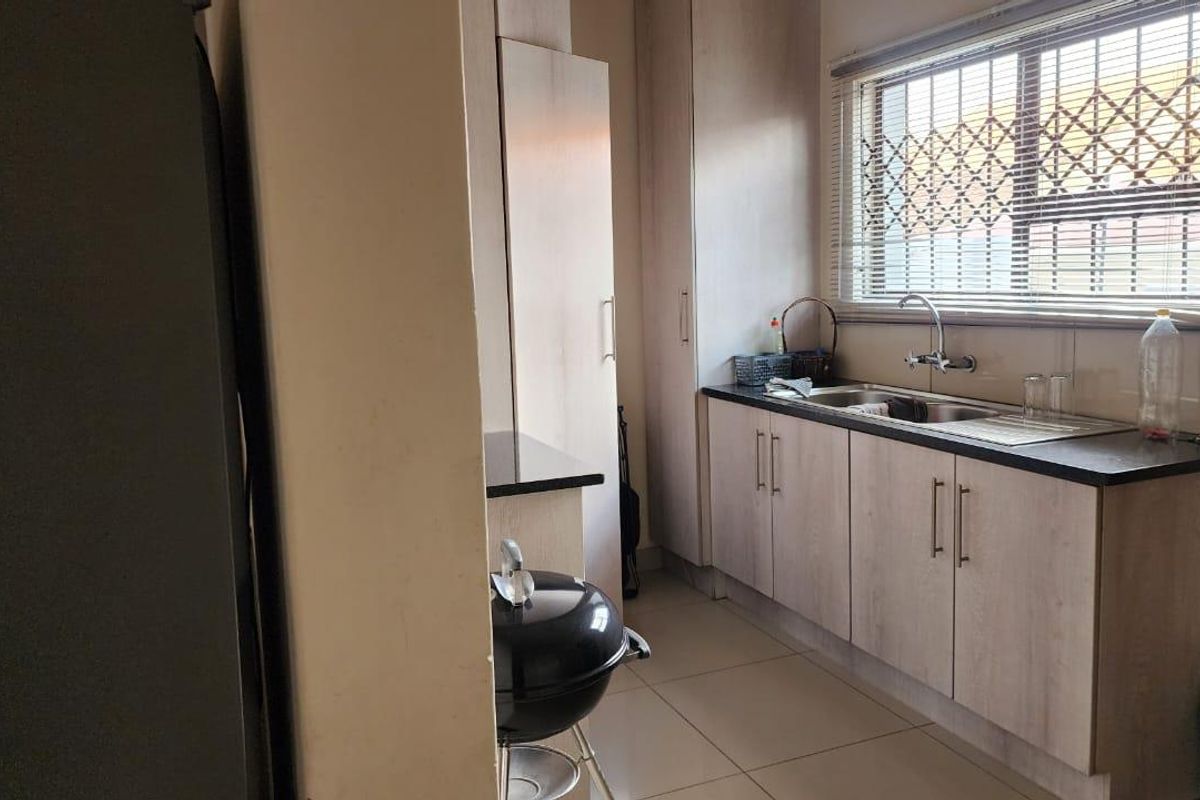 A functional kitchen featuring light wood-finish cabinetry, dark laminate countertops, a stainless steel sink, and tiled flooring with security bars on the window.