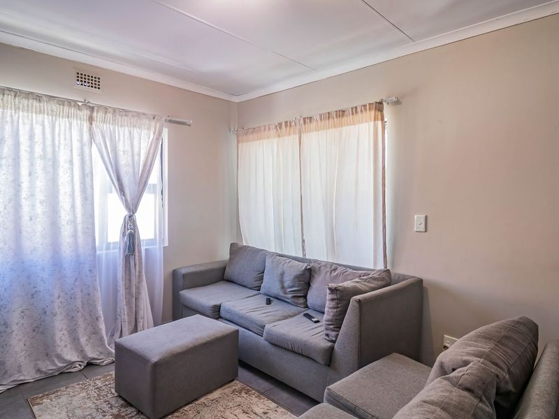 A neutrally painted living room featuring tiled flooring and dual windows with curtain fixtures.