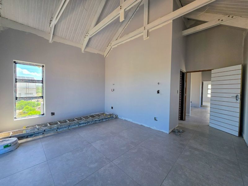 An unfinished bedroom featuring high vaulted ceilings with exposed timber trusses, large aluminium windows, and modern floor tiles, awaiting final touches.