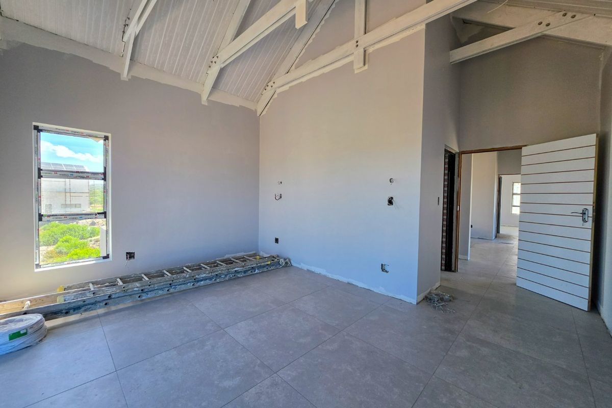 An unfinished bedroom featuring high vaulted ceilings with exposed timber trusses, large aluminium windows, and modern floor tiles, awaiting final touches.