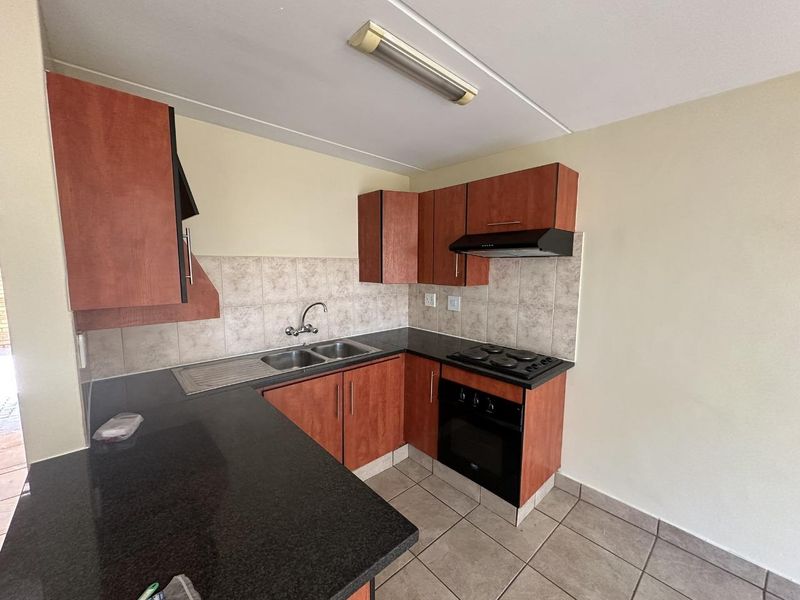 A functional kitchen featuring laminate cabinetry, granite countertops, a built-in oven with electric hob, and tiled backsplash and flooring.