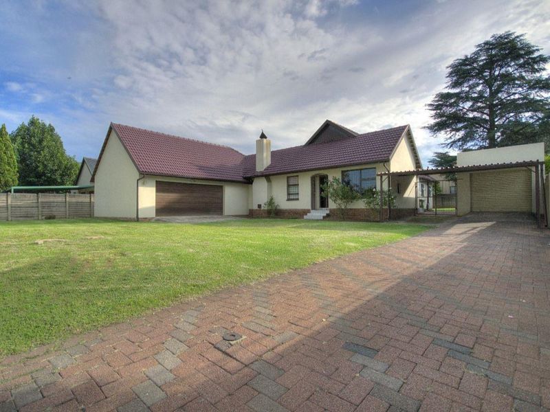 Front view of a residential property featuring a tiled roof, brick paved driveway, double garage, and an additional carport set within a spacious garden.