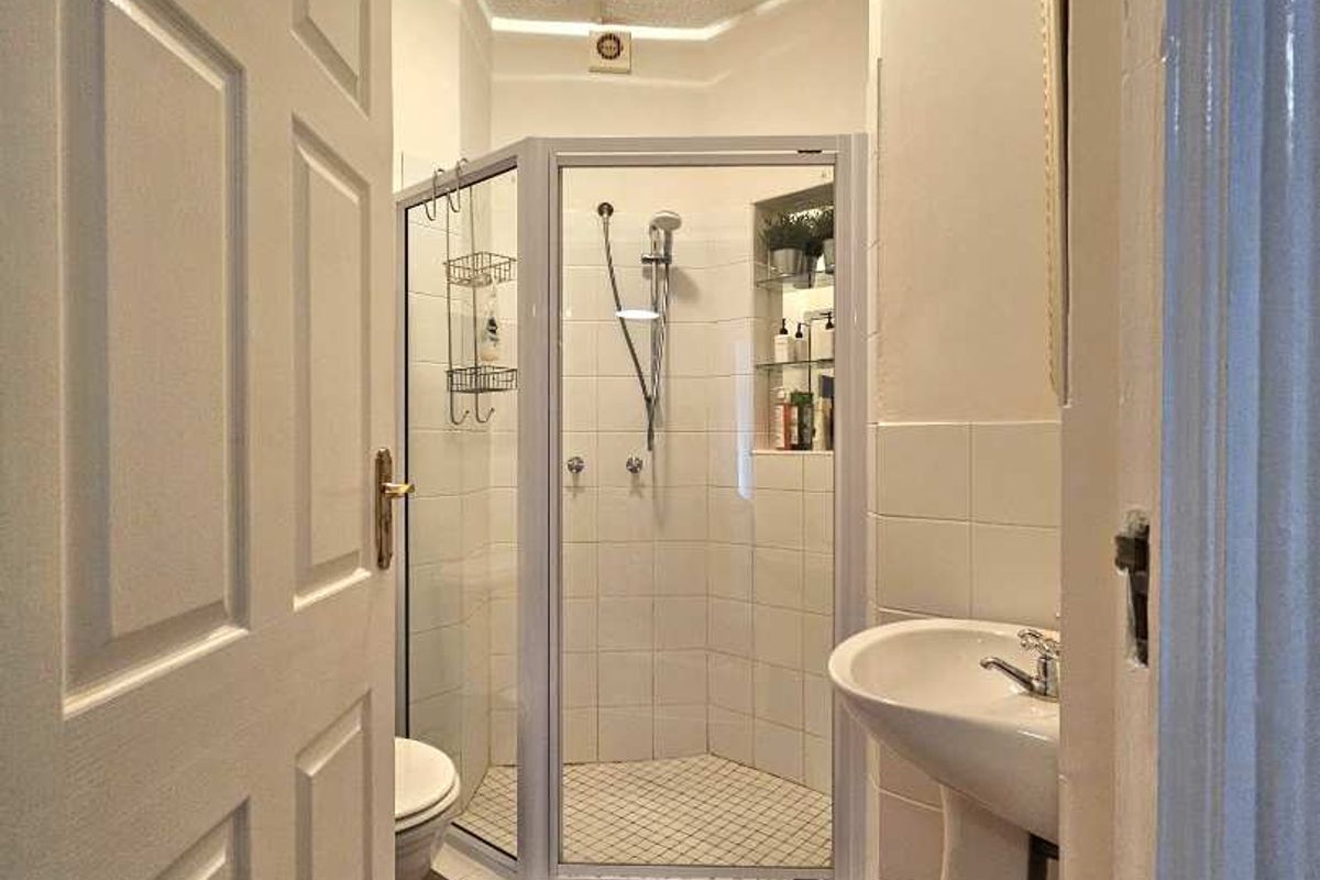 A compact bathroom featuring a corner shower enclosure, pedestal sink, and toilet with terracotta floor tiling.