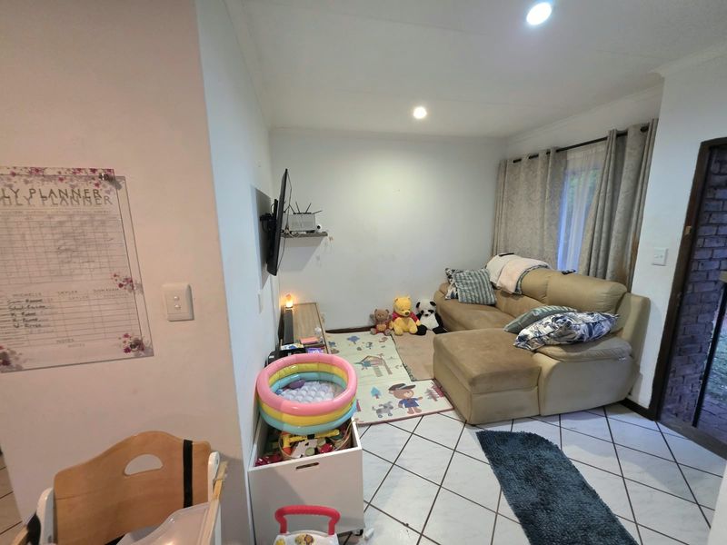 A living room area featuring tiled flooring, recessed downlighting, and a wall-mounted television bracket, providing a functional space for relaxation.