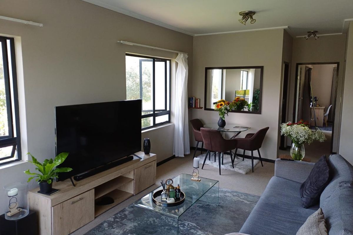 A comfortable living and dining area featuring neutral wall tones, carpeted flooring, and large windows that provide natural light.