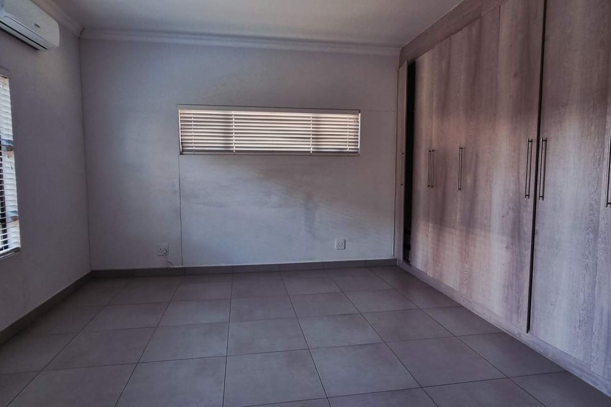A spacious bedroom featuring neutral floor tiles, built-in wooden cupboards, and a wall-mounted air conditioning unit.