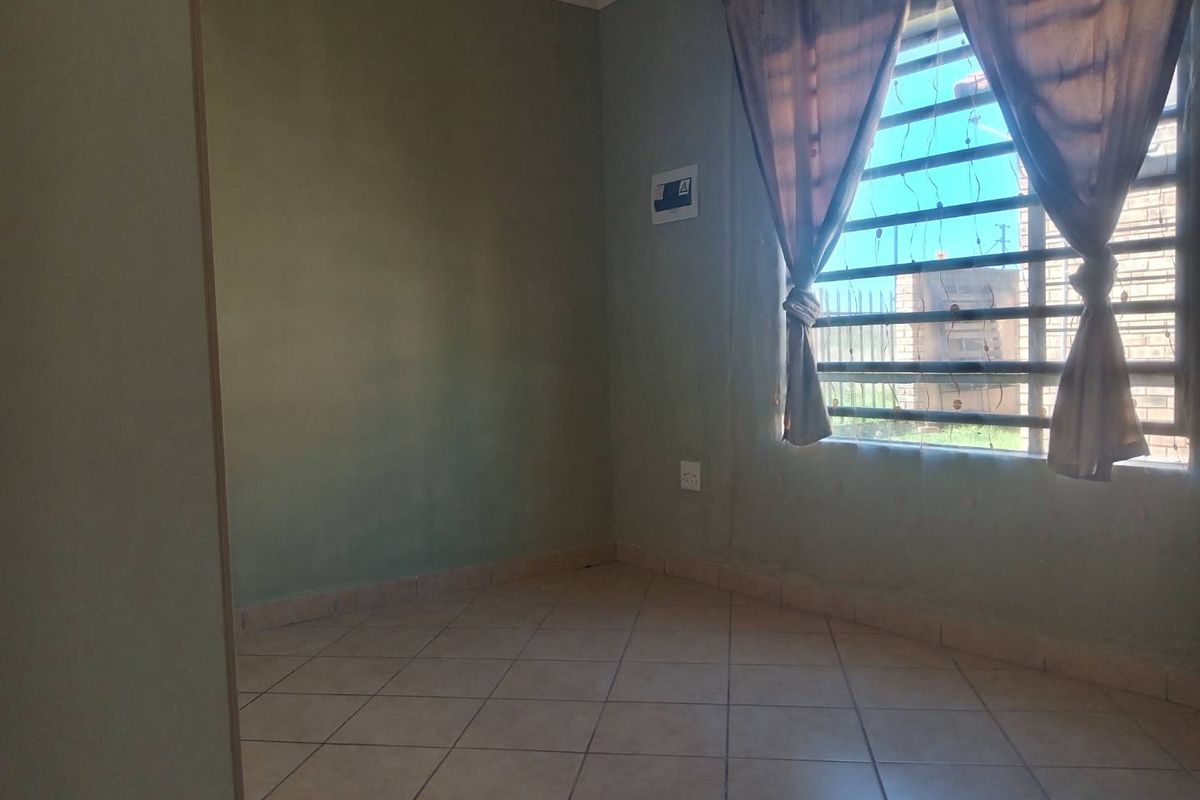 A compact, empty bedroom featuring tiled flooring and a window fitted with security bars.