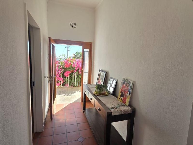 A bright hallway featuring terracotta floor tiles and an arched entrance leading to an outdoor balcony area.