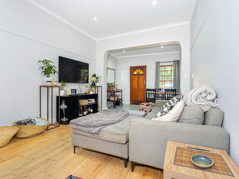 A bright living room featuring original timber flooring, a classic archway leading to the entrance, and recessed downlighting throughout the space.