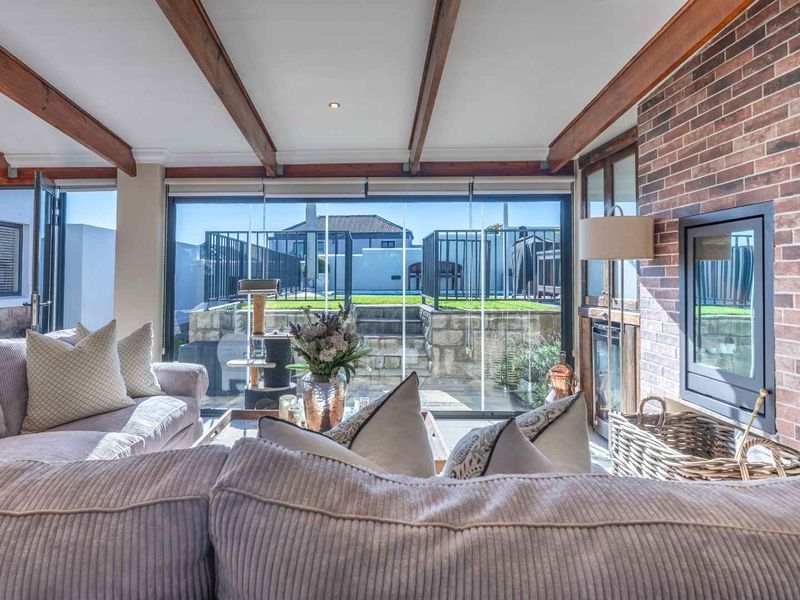 Inviting living room featuring exposed timber ceiling beams, a classic brick fireplace with a built-in insert, and seamless stacking glass doors opening to the garden.