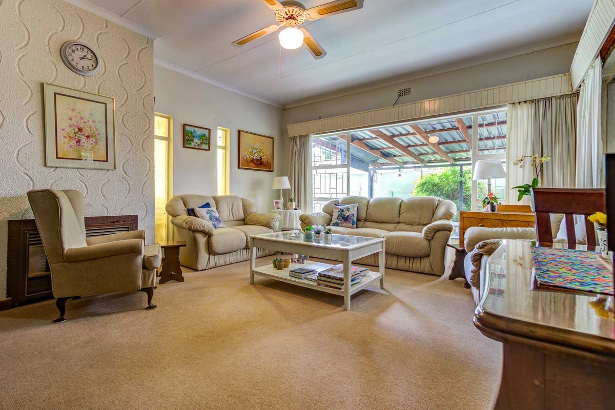 Spacious living room featuring a textured feature wall, ceiling fan, and large windows providing natural light and access to the outdoor patio area.