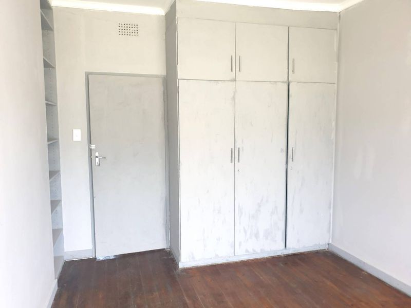 An empty bedroom featuring original wooden flooring, built-in cupboards with overhead storage, and integrated wall shelving.