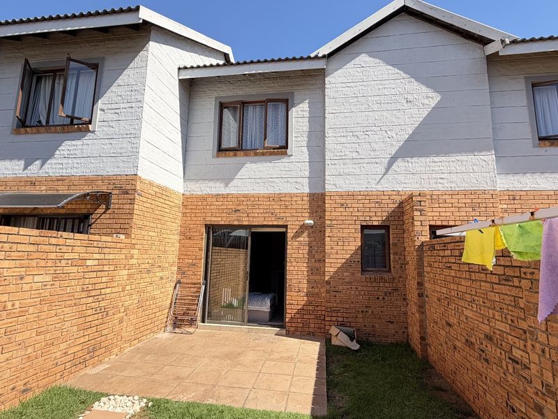 Rear view of a townhouse featuring a private brick-walled courtyard, tiled patio area, and sliding door access to the interior.